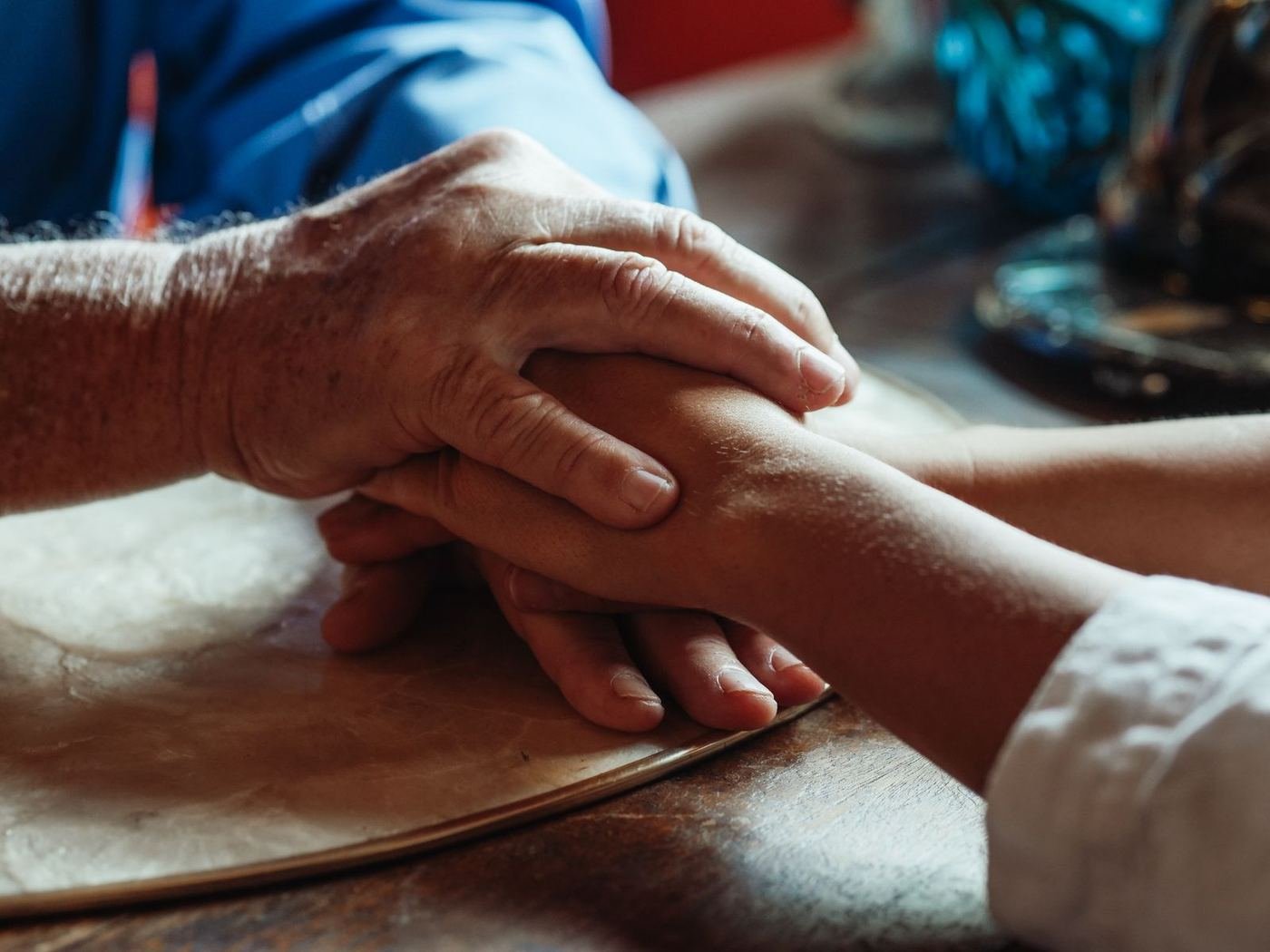 A grown child's hand resting gently over their aging parent's hand